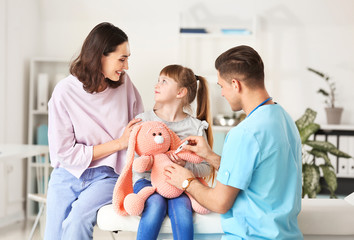 Pediatrician showing little girl how to use thermometer in clinic