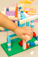 A child left hand playing with colorful plastic bricks at the tile floor