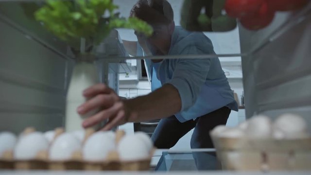 young man taking bottle of milk from fridge