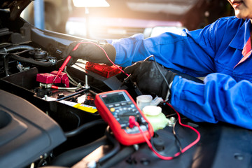 Femal technician uses multimeter voltmeter to check voltage level in car battery. Service and Maintenance car battery. - obrazy, fototapety, plakaty