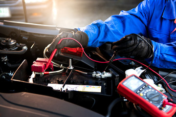Femal technician uses multimeter voltmeter to check voltage level in car battery. Service and...