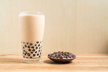 A glass cup of pearl milk tea (also called bubble tea) and a plate of tapioca ball on wooden background. Pearl milk tea is the most representative drink in Taiwan. Taiwan food . With copy space.