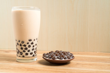 A glass cup of pearl milk tea (also called bubble tea) and a plate of tapioca ball on wooden background. Pearl milk tea is the most representative drink in Taiwan. Taiwan food . With copy space.