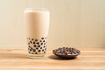A glass cup of pearl milk tea (also called bubble tea) and a plate of tapioca ball on wooden background. Pearl milk tea is the most representative drink in Taiwan. Taiwan food . With copy space.