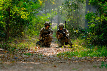 Two soldiers with the fighting uniform sit on the ground and discuss together for the battle in jungle.