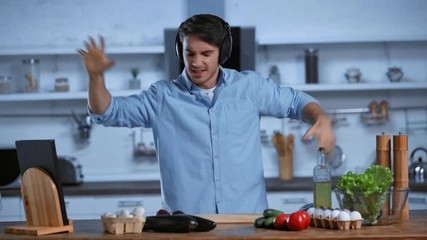 excited man in wireless headphones dancing near table with fresh ingredients