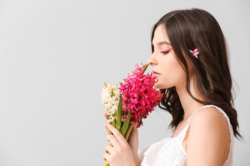 Beautiful young woman with hyacinth flowers on light background