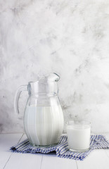 A jug of milk and a glass of milk on a light wooden table on a gray background. Concept of healthy natural products.