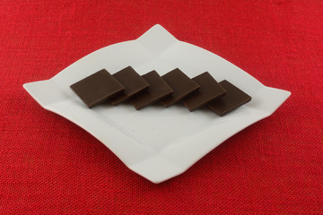 Dark chocolate squares on white dessert plate on red tablecloth