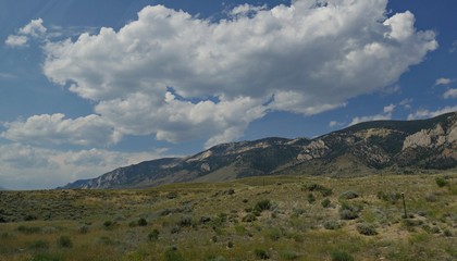 Wide upward shot of mountainside view with thick cotton clouds in the skies along North Fork Highway in Wyoming.