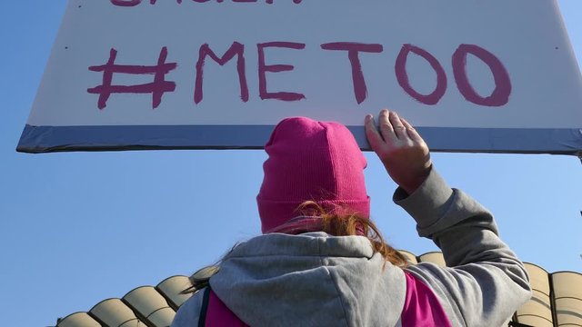 Low angle rear back shot of a girl holding a #MeToo sign with blue sky in background