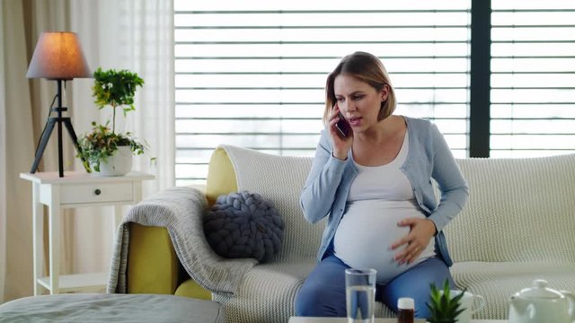 Portrait of pregnant woman in pain indoors at home, making emergency call.