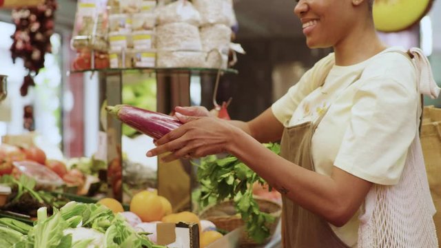 Smiling woman shopping a fresh eggplant at a market stand