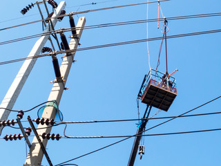 The electrician is working on the crane and the power lines on the blue sky background.