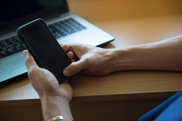 The man sitting on the table and his office is used smartphone and notebook computer at work.