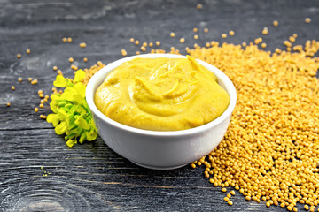 Sauce mustard in bowl with seeds and flower on black board