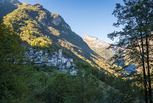 A scenic view of the old town of Corippo on a hill surrounded by forest and mountain ranges in Ticino, Switzerland