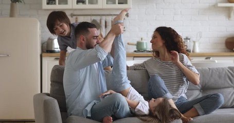 Happy family of four mum dad with cute little children son daughter tickling laughing on sofa together, parents and small kids having fun play bonding at home enjoy funny lifestyle activity on couch - Powered by Adobe