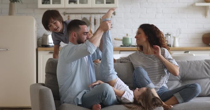 Happy family of four mum dad with cute little children son daughter tickling laughing on sofa together, parents and small kids having fun play bonding at home enjoy funny lifestyle activity on couch - Powered by Adobe