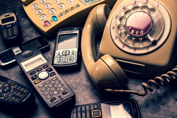 An old telephone with rotary dial, landline and obsoleted cellphone on a grunge background.