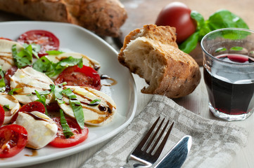 a plate with caprese salad together with bread and wine