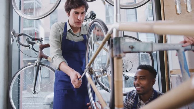 Multi-cultural team of trainees in workshop checking wheels on hand built bicycle frame together - shot in slow motion