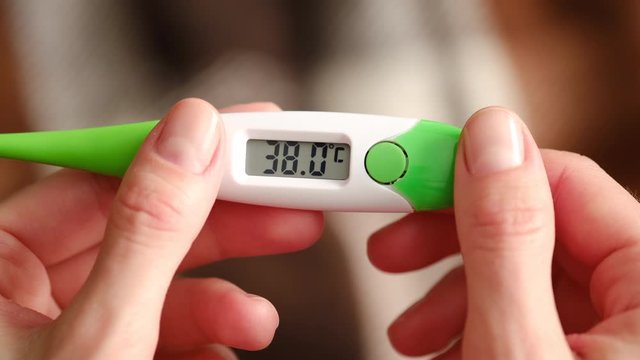 female with flu measures the temperature and looks at the thermometer in her hand. A used thermometer with a high temperature of a person with a coronavirus. 38 degrees