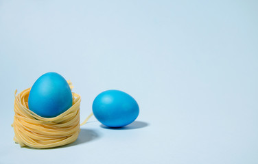 A blue egg in a nest stands against a blue background. In the background lies a blue egg. Minimalism, hard shadows