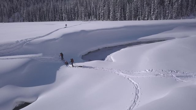 Advancing aerial: Expedition skiers with pulk sleds cross snowy river