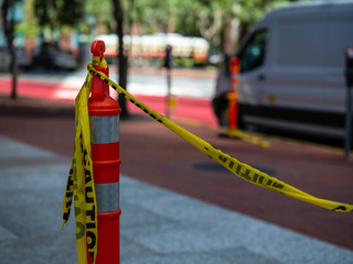 Yellow caution tape tied to orange safety cone on sidewalk with van in background
