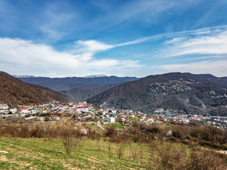 Fototapeta na wymiar View of the outskirts of the city from above in sunny weather. Houses and mountains under a blue cloudy sky. Caucasus mountains.
