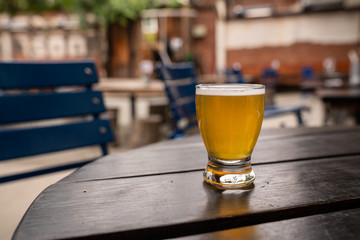 Golden beer in small tasting glass on table at outdoor restaurant