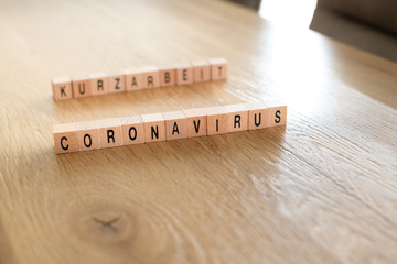 Konzeptbild: Coronavirus und Kurzarbeit, Wörter aus Holzwürfeln auf einem Konferenztisch