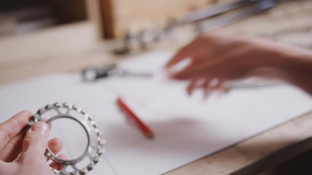 Close up of engineer in workshop measuring components for bicycle with micrometer and writing details on plan