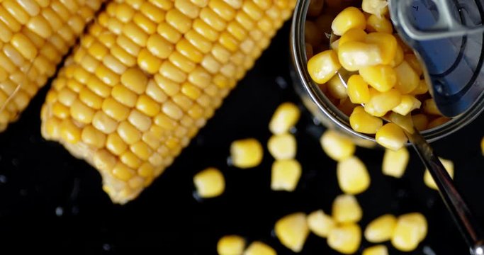 The man's hand pulls out a spoon of canned corn from cans.