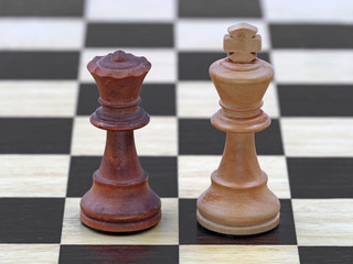 Chess black queen and white king stand on a wooden chessboard