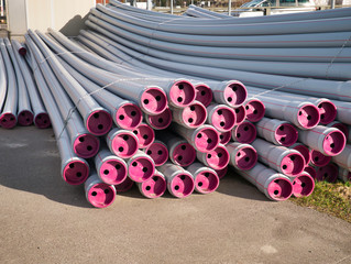New, gray sewer pipes bundled with cords made of gray plastic with magenta colored lids are ready for laying next to the street.