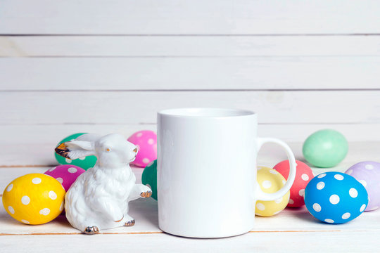 White coffee mug with Easter egga and bunny on pink wooden background.