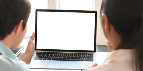 Behind shot of business people working together with white blank screen computer laptop while sitting together at black working desk over modern office as background.