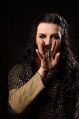 A dark-haired woman with a dirk, a Scandinavian warrior in a chain mail against a dark background