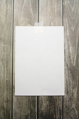A white sheet of A4 paper hanging on a wall glued with a piece of paper tape on a wooden background.