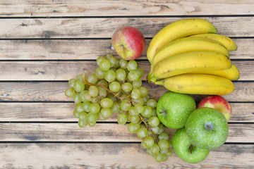 top view on fruits bananas, grapes and apples on wooden background