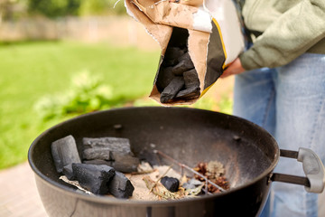 cooking, heat and fire concept - close up of man charcoal pouring burning to brazier outdoors