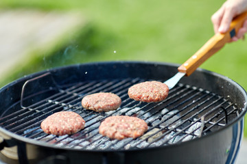 cooking, barbecue and fast food concept - close up of burger meat cutlets roasting on brazier grill outdoors