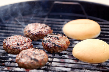 cooking, barbecue and fast food concept - close up of burger meat cutlets roasting on brazier grill outdoors