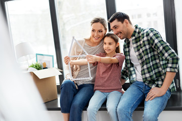 mortgage, family and real estate concept - happy mother, father and little daughter with folding ruler in shape of house and stuff in boxes moving to new home