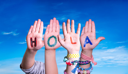 Kids Hands Holding Colorful Spanish Word Hola Means Hello. Blue Sky As Background