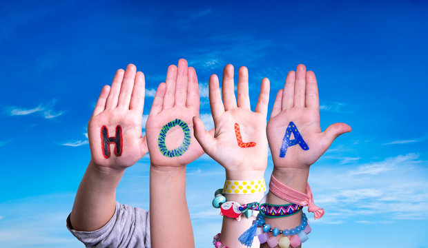 Kids Hands Holding Colorful Spanish Word Hola Means Hello. Blue Sky As Background