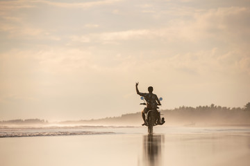 Surfer with surfboard on motorbike at sunset beach © cppzone