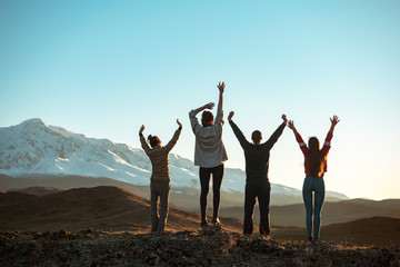 Four happy friends stands with raised arms in mountains